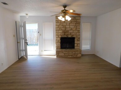 Unfurnished living room with wood finished floors, a ceiling fan, a fireplace, and a textured ceiling