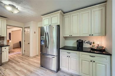 Kitchen featuring stainless steel fridge with ice dispenser, cream cabinetry, dark countertops, light updated flooring, and a textured ceiling