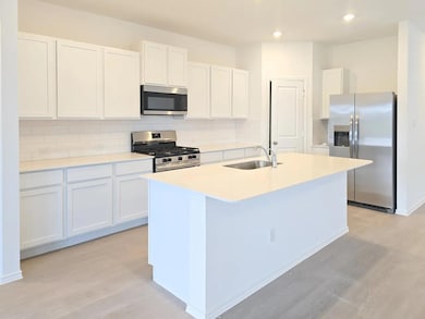 Kitchen featuring stainless steel appliances, tasteful backsplash, white cabinetry, a center island with sink, and light wood finished floors