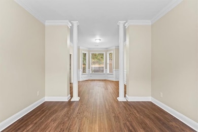 Spare room featuring ornamental molding, dark wood finished floors, and ornate columns