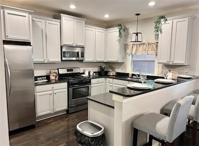 Kitchen with a peninsula, appliances with stainless steel finishes, hanging light fixtures, a breakfast bar area, and dark wood-style flooring