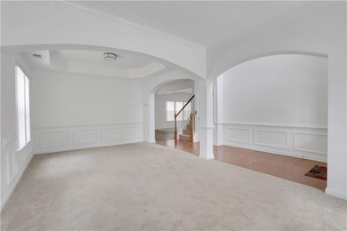 Carpeted spare room featuring a decorative wall, ornamental molding, arched walkways, stairs, and wainscoting