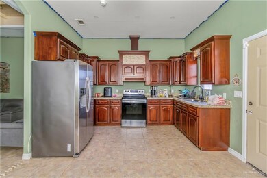 Kitchen with custom exhaust hood, light stone counters, light tile flooring, appliances with stainless steel finishes, and sink