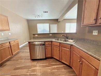 Kitchen featuring stainless steel dishwasher, light wood-style floors, a textured ceiling, a peninsula, and brown cabinetry