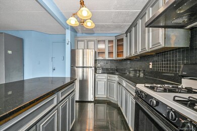 Kitchen with ventilation hood, gas stove, freestanding refrigerator, dark stone countertops, and hanging light fixtures