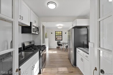 Kitchen featuring appliances with stainless steel finishes, white cabinets, light wood-type flooring, dark stone countertops, and wainscoting