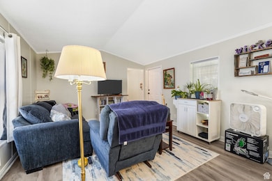 Living area with ornamental molding, wood finished floors, and lofted ceiling