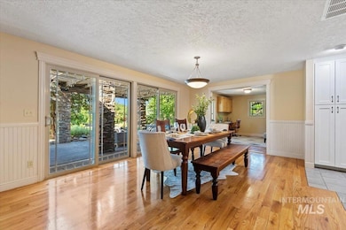 Dining area featuring light wood-type flooring, plenty of natural light, wainscoting, and a textured ceiling