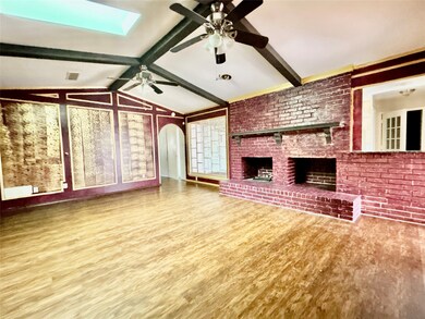 Unfurnished living room with light wood-style floors, a skylight, arched walkways, a brick fireplace, and brick wall