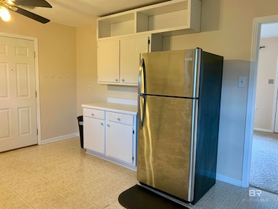 Kitchen with white cabinetry, ceiling fan, stainless steel fridge, and light colored carpet