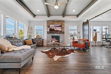 Living room featuring a barn door, wood finished floors, beamed ceiling, a fireplace, and a ceiling fan