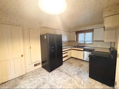 Kitchen featuring black appliances, wallpapered walls, and white cabinets