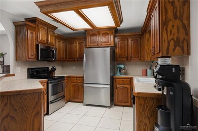 Kitchen with tile counters, light tile patterned floors, appliances with stainless steel finishes, decorative backsplash, and sink