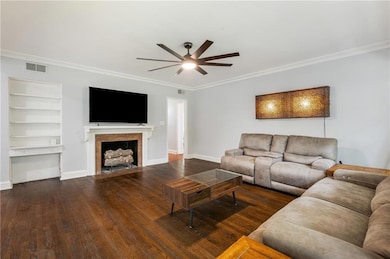 Living area with crown molding, dark wood-style floors, a fireplace with flush hearth, and a ceiling fan