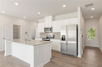 Kitchen with stainless steel appliances, a sink, a center island with sink, light wood finished floors, and backsplash
