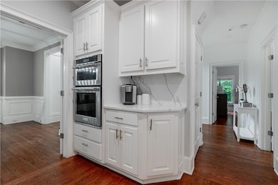 Kitchen with stainless steel double oven, crown molding, white cabinets, dark wood-type flooring, and backsplash