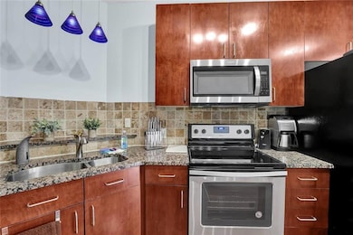 Kitchen featuring appliances with stainless steel finishes, a sink, light stone countertops, tasteful backsplash, and brown cabinets