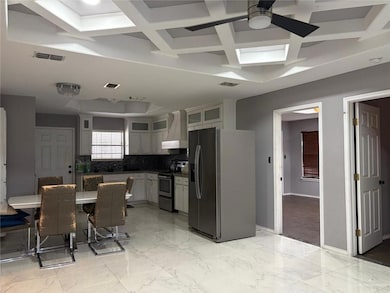 Kitchen featuring appliances with stainless steel finishes, wall chimney range hood, coffered ceiling, a ceiling fan, and dark countertops