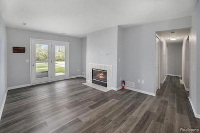 Unfurnished living room with a tiled fireplace and dark wood-type flooring