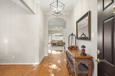 Step inside to a bright, open foyer featuring wood flooring, high ceilings, crown molding, and a stylish light fixture with natural light flowing from the back of the home.