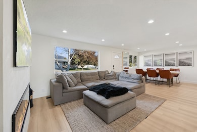 Living room with a lit fireplace, plenty of natural light, light wood finished floors, and recessed lighting