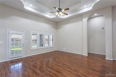 Spare room with a tray ceiling, a ceiling fan, wood finished floors, arched walkways, and a high ceiling