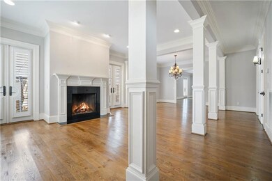 Unfurnished living room with wood finished floors, a lit fireplace, ornamental molding, a chandelier, and ornate columns