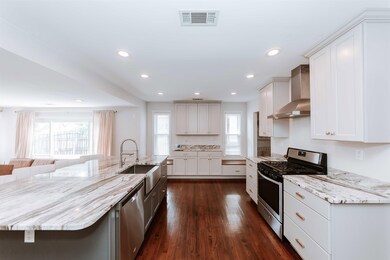 Kitchen featuring appliances with stainless steel finishes, wall chimney exhaust hood, a sink, light stone countertops, and dark wood finished floors
