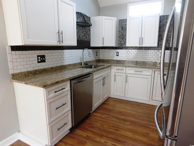 Kitchen featuring a sink, white cabinetry, dark wo
