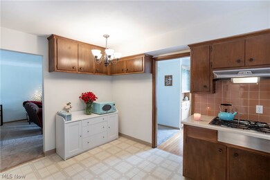 Kitchen with hanging light fixtures, light tile flooring, backsplash, an inviting chandelier, and stainless steel gas stovetop