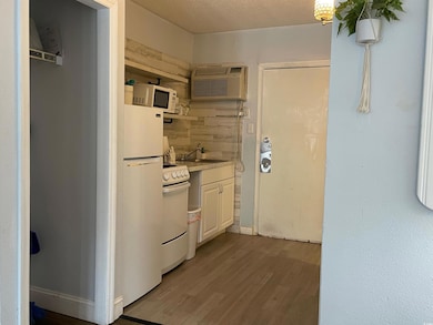 Kitchen with white appliances, a wall unit AC, wood finished floors, light countertops, and a sink