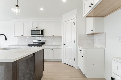 Kitchen with white cabinetry, decorative light fixtures, recessed lighting, stainless steel appliances, and light wood finished floors