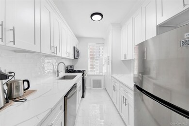 Kitchen with appliances with stainless steel finishes, white cabinetry, light stone counters, light marble finish flooring, and tasteful backsplash