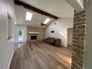 Unfurnished living room with a textured wall, a skylight, light wood-style floors, a fireplace, and ceiling fan