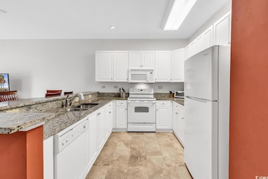 Kitchen with a peninsula, white appliances, white cabinets, and dark stone counters