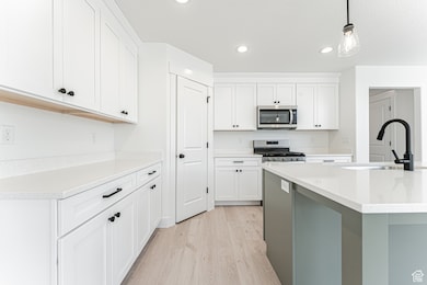 Kitchen featuring light wood-style flooring, stainless steel appliances, recessed lighting, white cabinetry, and decorative light fixtures