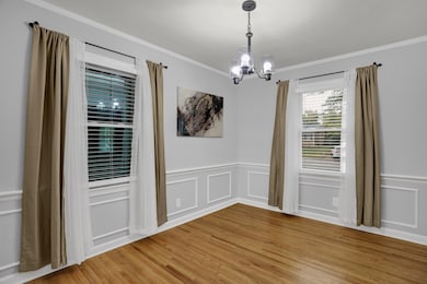 Unfurnished dining area featuring ornamental molding, light wood finished floors, a chandelier, wainscoting, and a decorative wall
