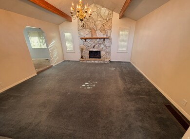 Unfurnished living room with arched walkways, dark carpet, beamed ceiling, a stone fireplace, and a chandelier