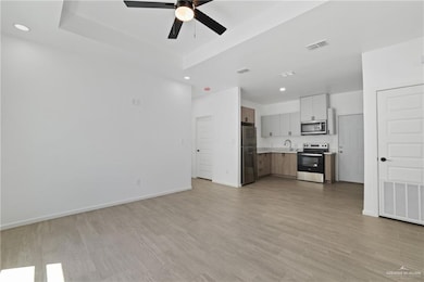 Unfurnished living room featuring a tray ceiling, ceiling fan, a sink, and visible vents