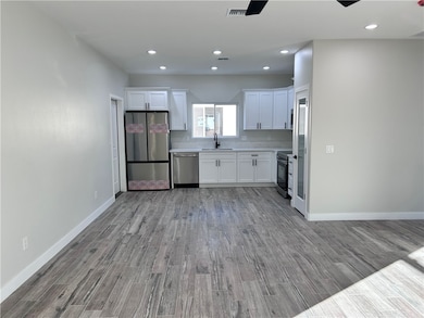 Kitchen featuring white cabinets, appliances with stainless steel finishes, dark wood-style flooring, light countertops, and recessed lighting