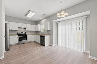 Kitchen featuring appliances with stainless steel finishes, white cabinets, decorative light fixtures, a chandelier, and light wood-type flooring