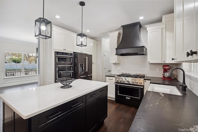 Kitchen with custom range hood, dark cabinetry, a sink, white cabinets, and black appliances