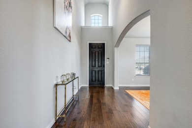 Foyer entrance featuring arched walkways, dark wood-style floors, a towering ceiling, and a textured wall