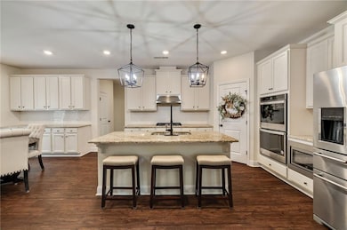 Kitchen with stainless steel appliances, under cabinet range hood, backsplash, a breakfast bar area, and recessed lighting