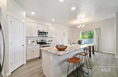 Kitchen featuring appliances with stainless steel finishes, light wood-type flooring, a chandelier, an island with sink, and a breakfast bar