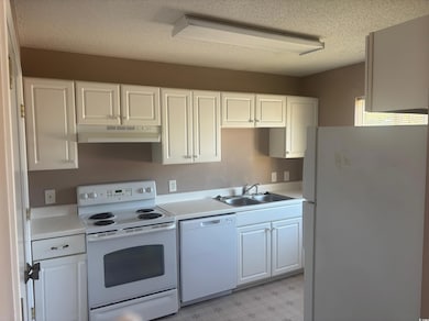 Kitchen featuring white appliances, light countertops, white cabinets, and a textured ceiling