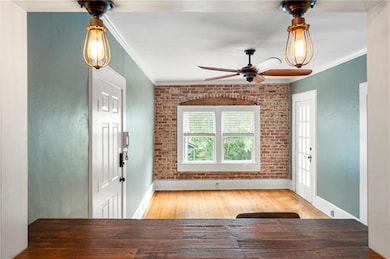 Entryway featuring crown molding, baseboards, ceiling fan, wood finished floors, and brick wall