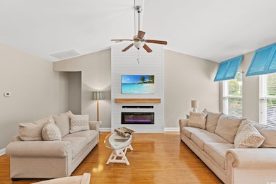 Living room with light wood-type flooring, a ceiling fan, a fireplace, and lofted ceiling
