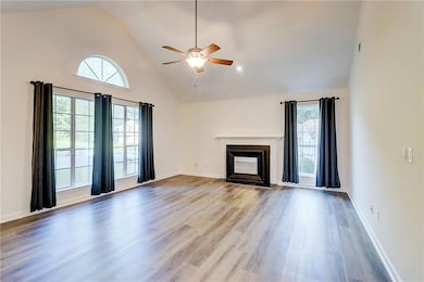Unfurnished living room with a ceiling fan, wood finished floors, a fireplace with flush hearth, and high vaulted ceiling