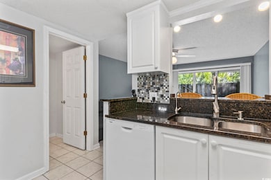 Kitchen with white cabinetry, dishwasher, light tile patterned flooring, dark stone countertops, and a textured ceiling